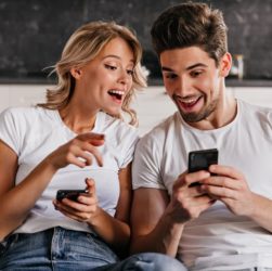 coppia-sorridente-seduto-sul-divano-con-i-telefoni-giovane-donna-che-tiene-smartphone
